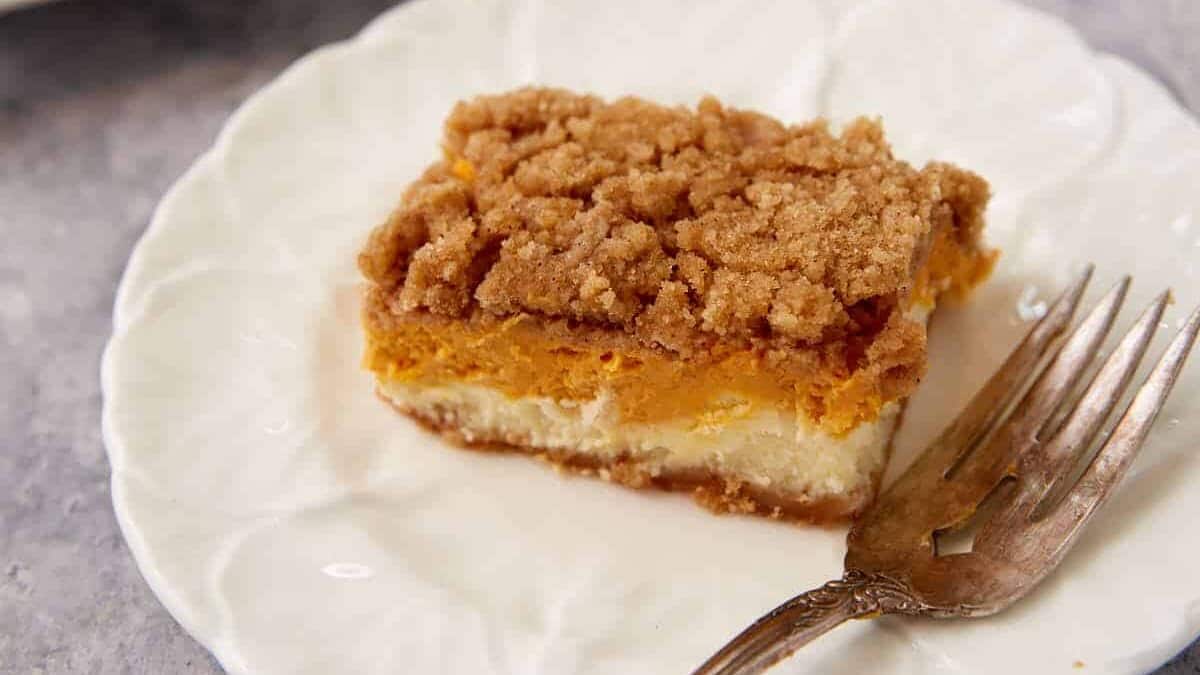 A pumpkin cheesecake bar on a plate with a fork.