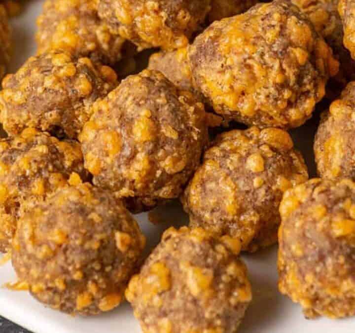 A white platter of keto sausage balls next to a bowl of dip.