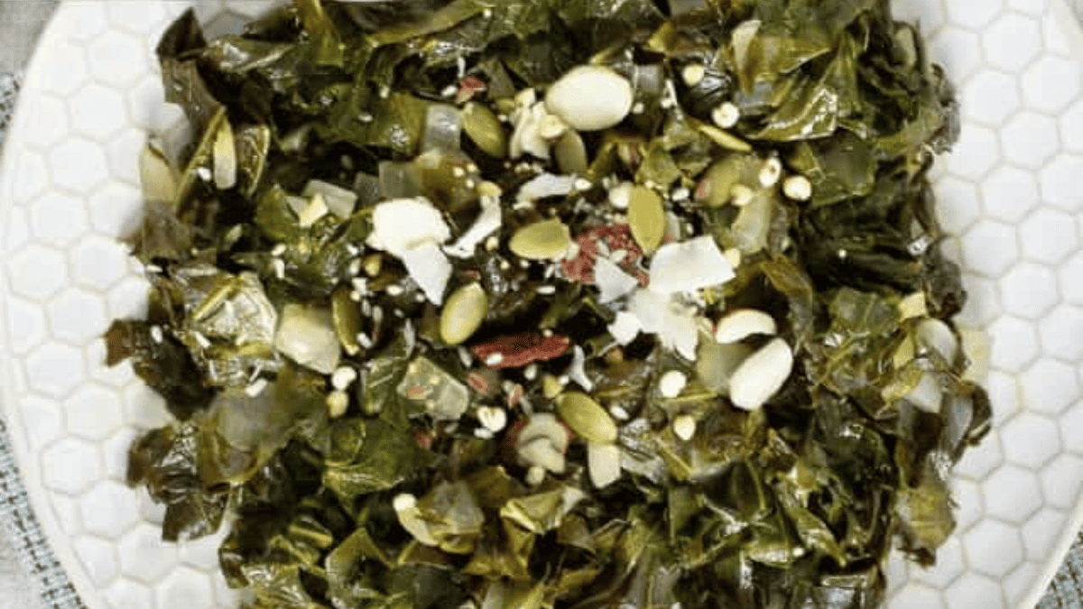 A plate of cooked leafy greens, topped with seeds, nuts, and shredded coconut, served on a white hexagonal-patterned plate—an elegant option for your Thanksgiving dinner ideas.