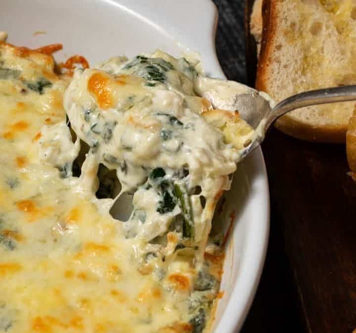 A baking dish of spinach artichoke dip with a spoon in the side.