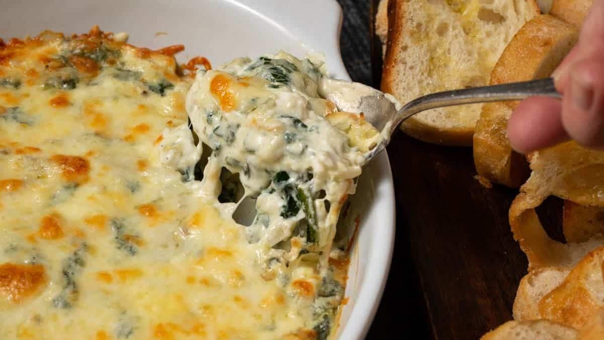 A baking dish of spinach artichoke dip with a spoon in the side.