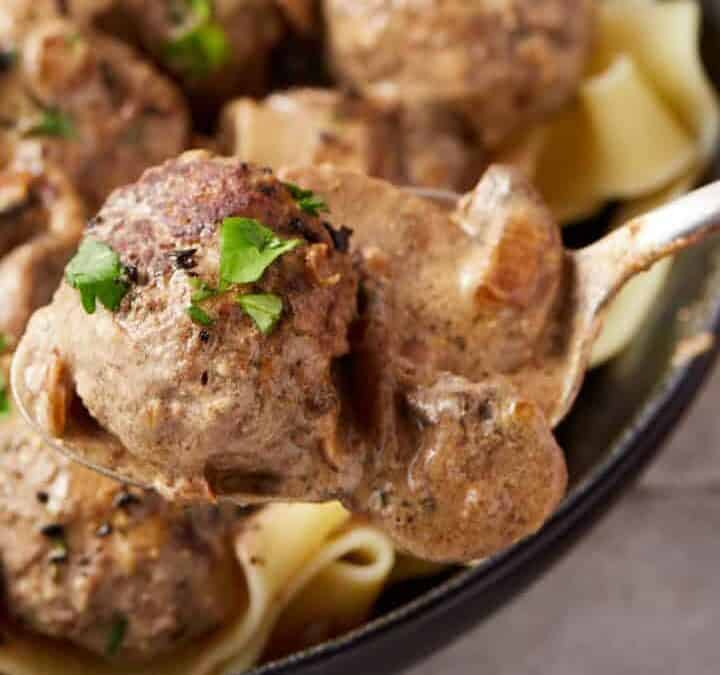 A bowl of egg noodles covered in stroganoff meatballs.