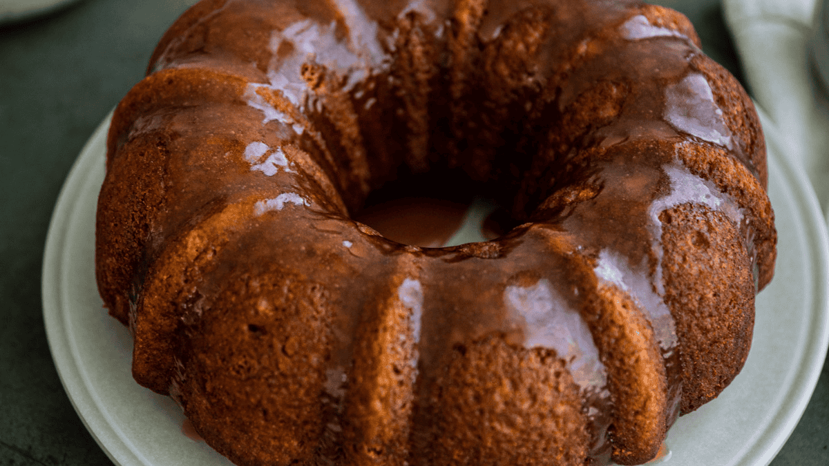 A glazed bundt cake sits on a white plate, its surface golden brown with a shiny, thin layer of icing drizzled over the top and sides—a beautiful example of pumpkin desserts.