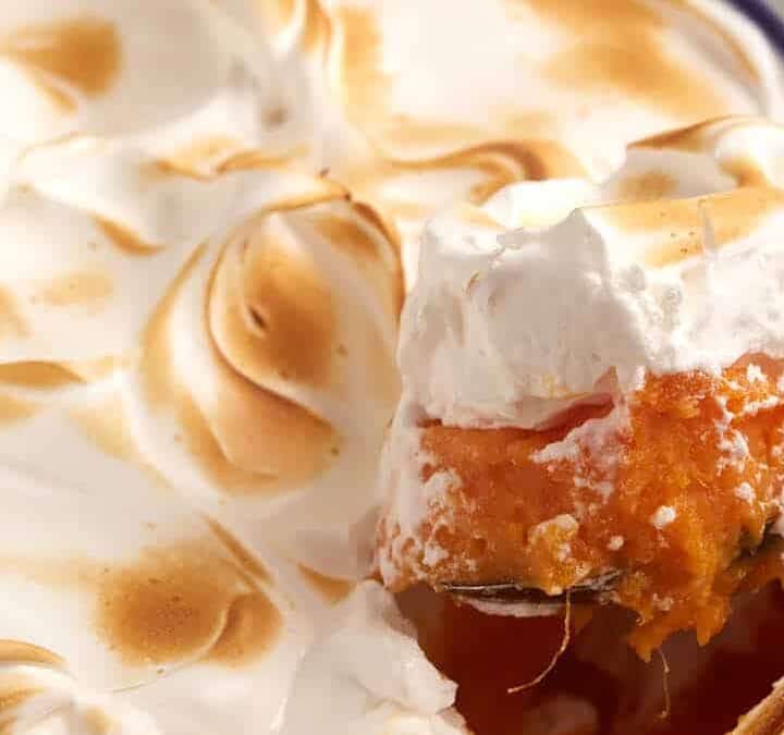 A spoon dipping out a portion of sweet potato casserole with marshmallow topping.