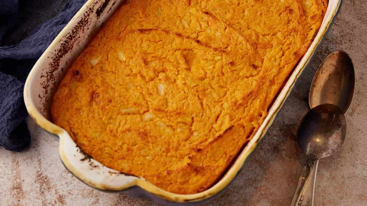 A baked sweet potato souffle in a casserole dish next to serving spoons.
