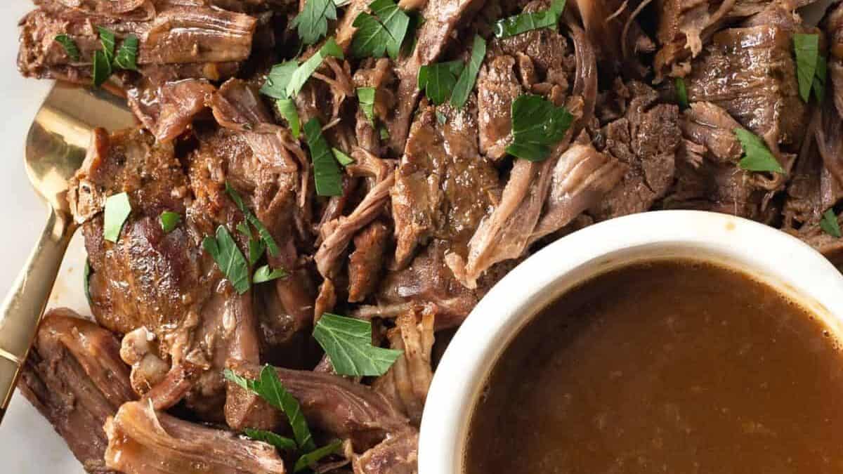 A platter of roast beef next to a bowl of gravy.