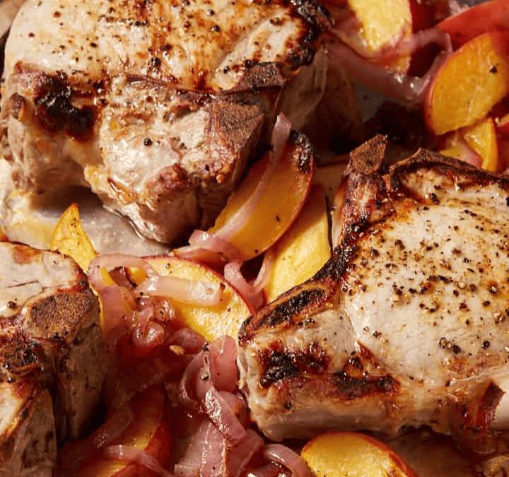 Three seasoned pork chops on a baking sheet, surrounded by sliced peaches and red onions, all roasted and slightly caramelized—a perfect example of effortless sheet pan meals.