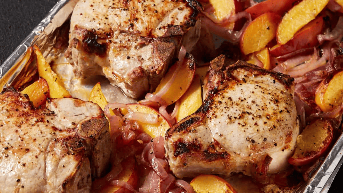 Three seasoned pork chops on a baking sheet, surrounded by sliced peaches and red onions, all roasted and slightly caramelized—a perfect example of effortless sheet pan meals.