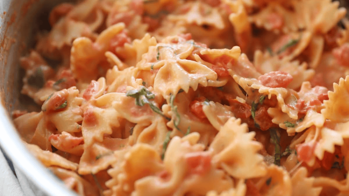 Close-up of farfalle (bow-tie) pasta covered in a creamy tomato sauce with bits of chopped herbs, served in a pan—a must-try for anyone who loves delicious pasta recipes.