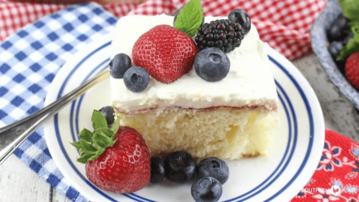 A slice of vanilla cake topped with whipped cream and assorted fresh berries—strawberries, blueberries, and blackberries—served on a white plate with a blue rim, perfect inspiration for holiday sheet cake recipes.