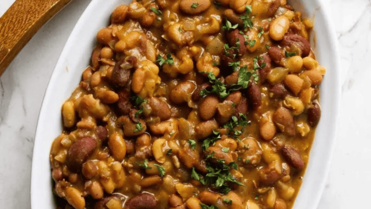 A white oval dish filled with baked beans in a thick, brown sauce, garnished with chopped fresh herbs on top—perfect as a cozy addition to your Christmas sides.