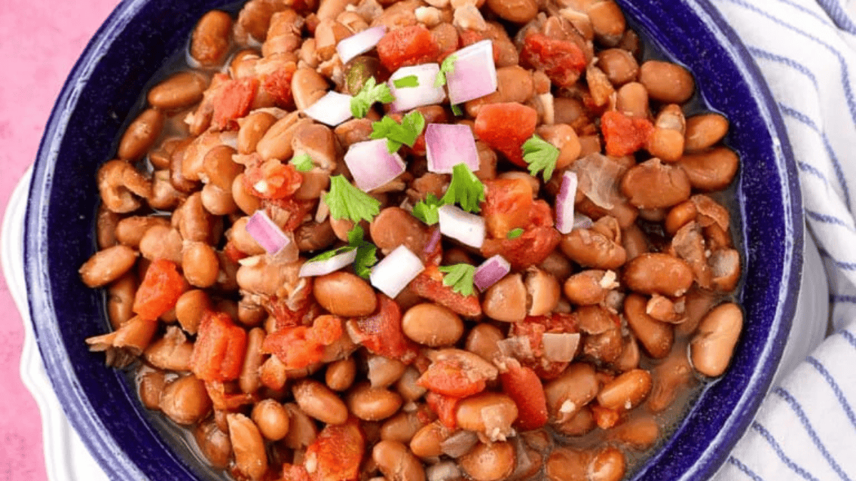 A bowl of pinto beans mixed with diced tomatoes, topped with chopped red onion and fresh cilantro, sits on a striped cloth—perfect for those seeking delicious veggie recipes.