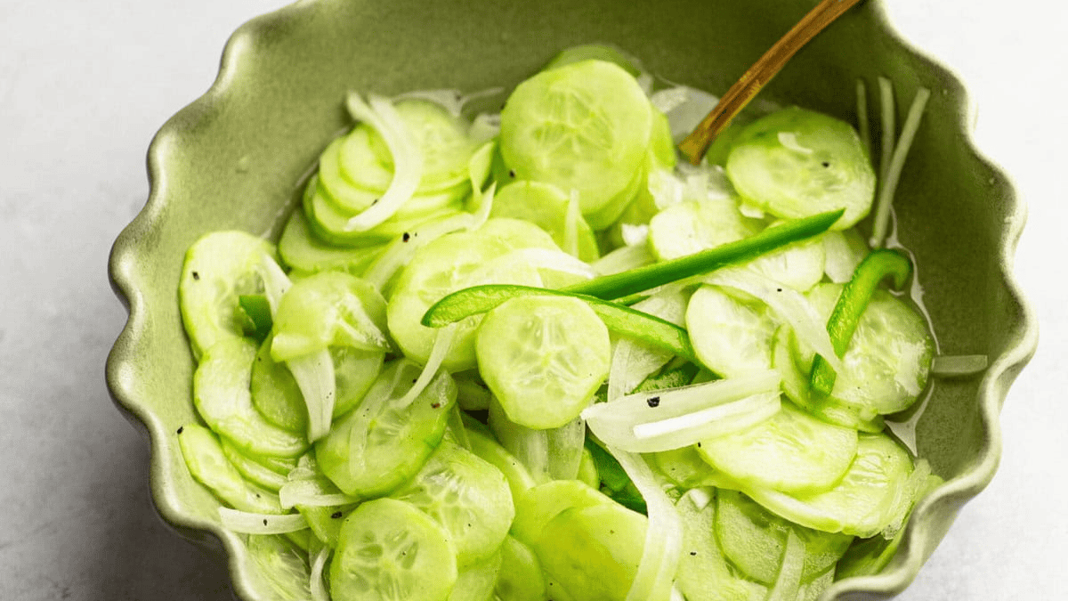 A bowl of sliced cucumbers with a wooden spoon.