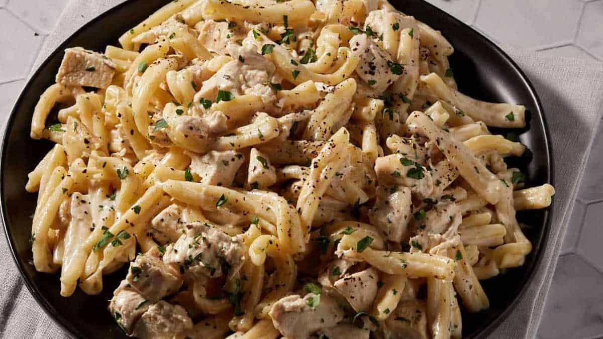 A black platter of lemony chicken pasta on a grey napkin.