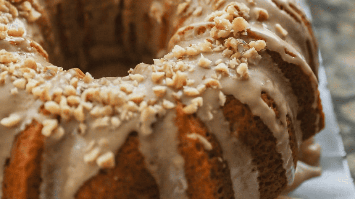 A close-up of a bundt cake topped with a white glaze and sprinkled with chopped nuts. Perfect for holiday cakes and cupcakes, the cake has a golden-brown crust and detailed ridges from the bundt pan.