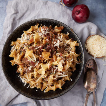 a bowl of pasta with sausage apples and onions.