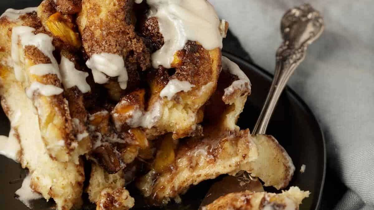 A serving of a peach cinnamon roll on a plate with a bite.