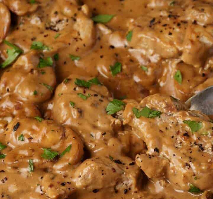 A serving spoon in a skillet of pork marsala medallions