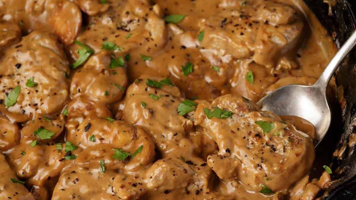 A serving spoon in a skillet of pork marsala medallions