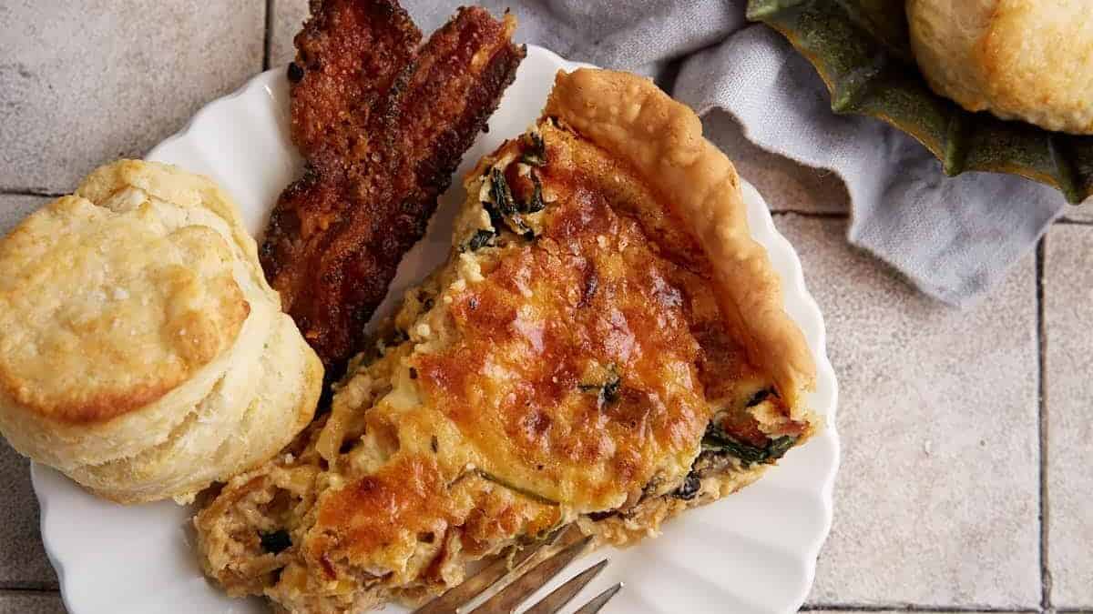 A slice of quiche next to a plate of biscuits.