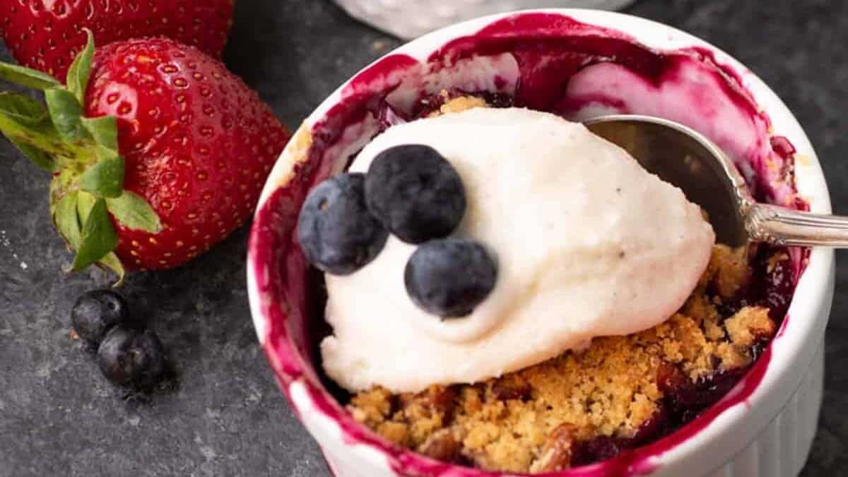 Rhubarb berry crisp in three ramekins with strawberries on the side.