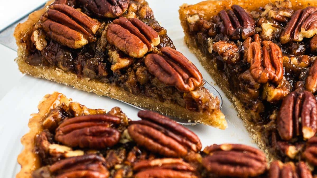 Close-up of sliced pecan pie with a golden brown crust, topped with whole and chopped pecans, displayed on a white plate—perfect inspiration for your Christmas pie recipes.