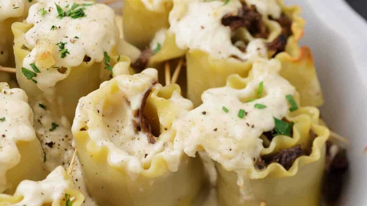 A casserole dish full of lasagna rolls covered in a cheese sauce.