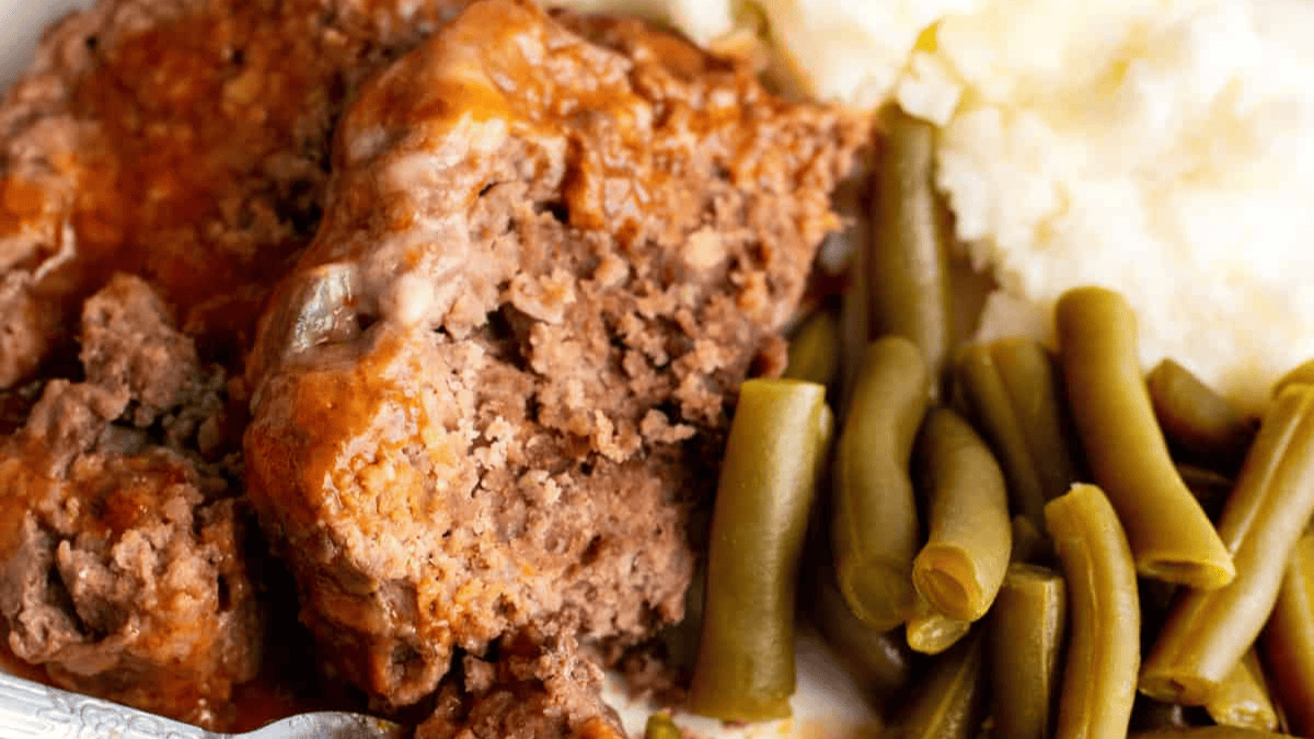 A close-up of a plate with meatloaf topped with sauce, green beans, and mashed potatoes—perfect inspiration for your Christmas dinner menu ideas.
