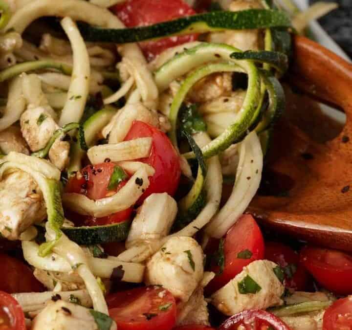 Zucchini noodles with cherry tomatoes on a white platter with a wooden spoon