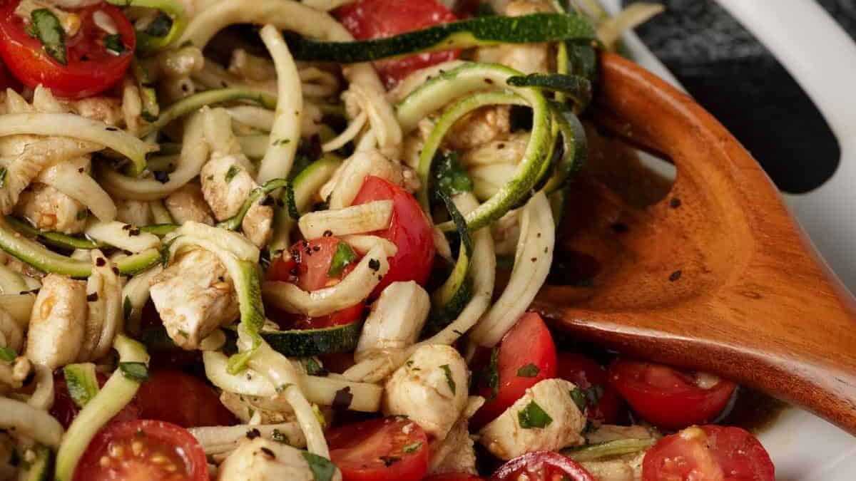 Zucchini noodles with cherry tomatoes on a white platter with a wooden spoon