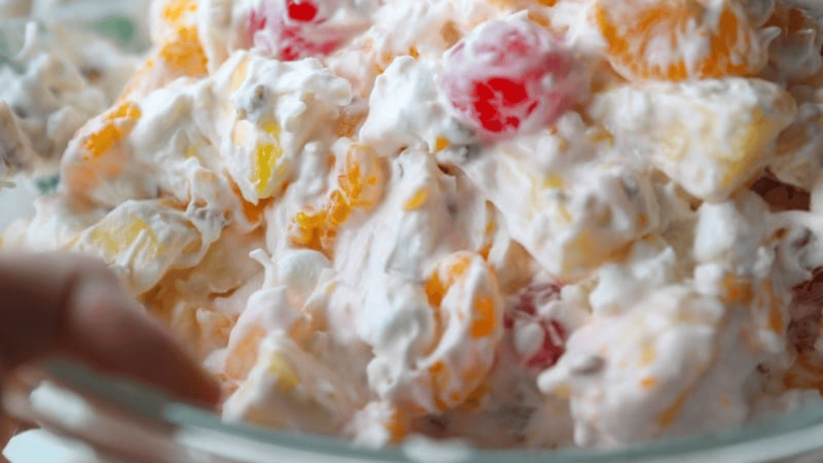 A close-up of a fruit salad mixed with whipped cream, showing colorful pieces of fruit like mandarin oranges and cherries coated in a creamy dressing—a delightful example of classic fruit dishes.