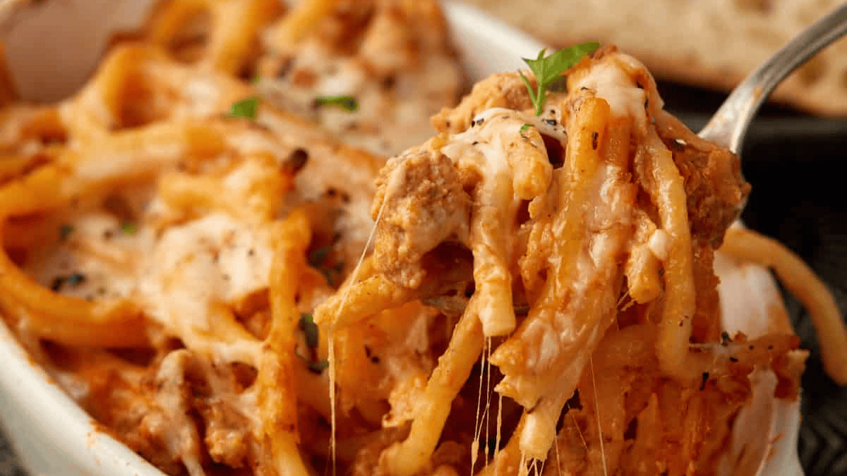 A close-up of a cheesy baked spaghetti casserole with tomato sauce and ground meat, topped with melted cheese and herbs, makes for one of those easy date night dinners—served with a fork lifting a gooey, delicious portion.