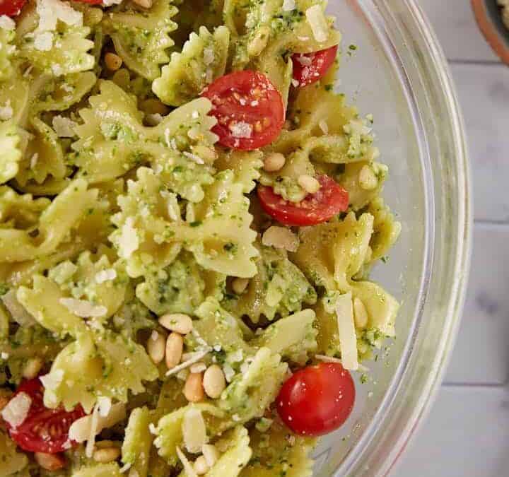 Delicious pesto pasta salad with fresh basil and cherry tomatoes in a glass bowl.