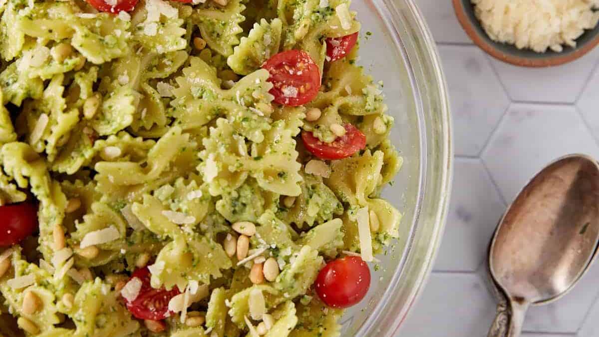 Delicious pesto pasta salad with fresh basil and cherry tomatoes in a glass bowl.