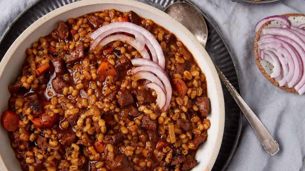 Beef and barley soup next to a plate of crackers.