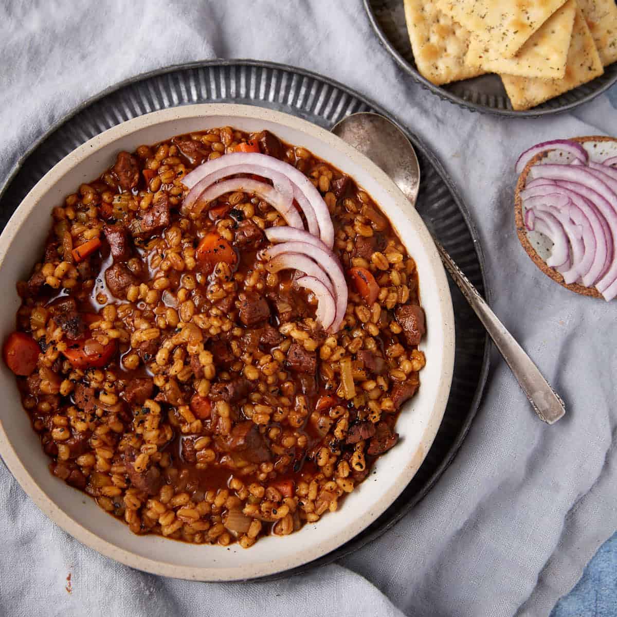 A bowl of beef and barley soup next to crackers.