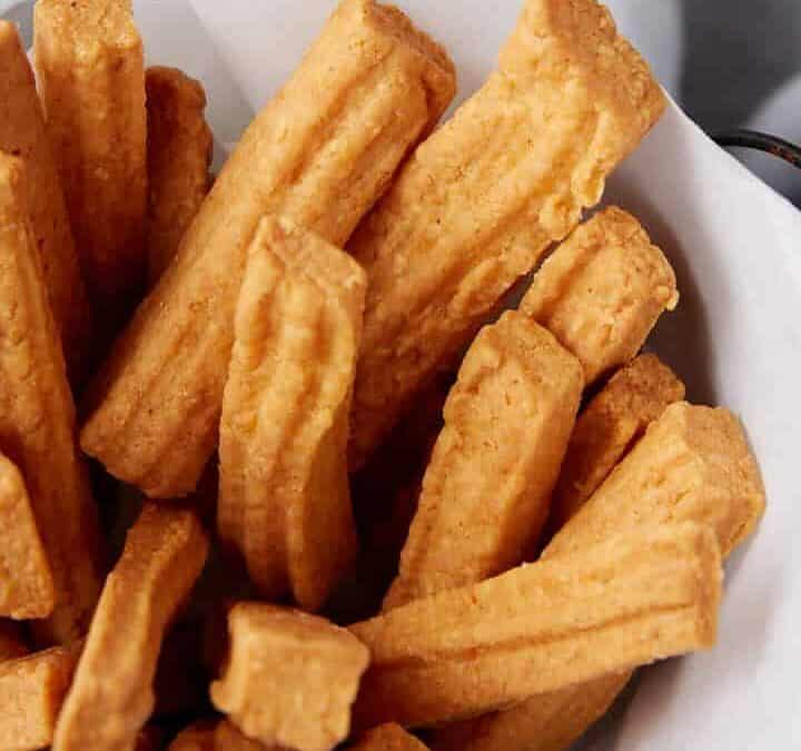 A basket of cheese straws next to glassesof wine.