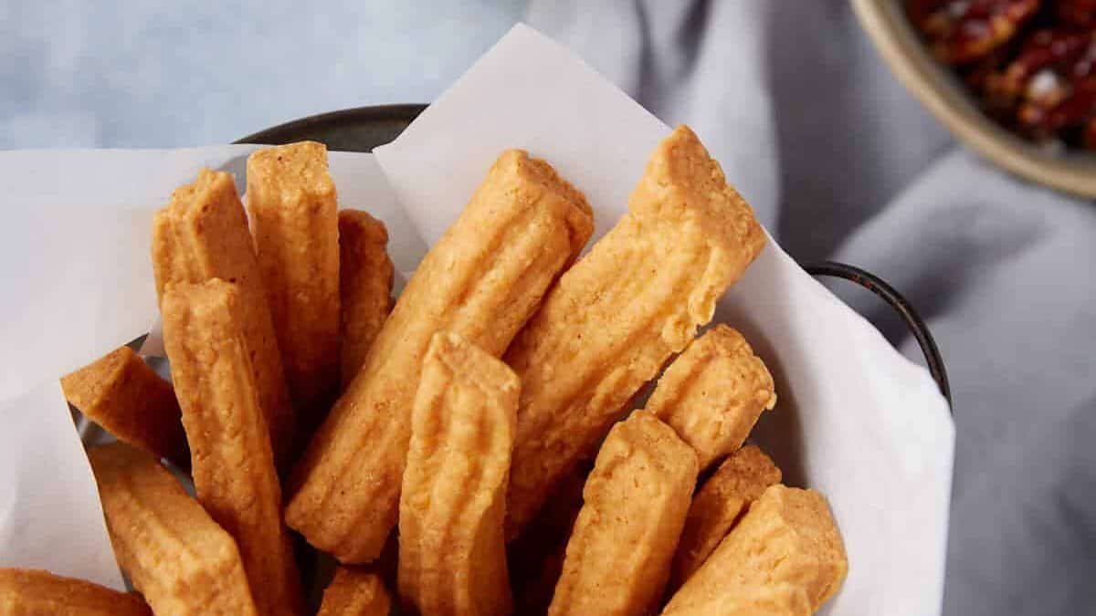 A basket of cheese straws next to glassesof wine.