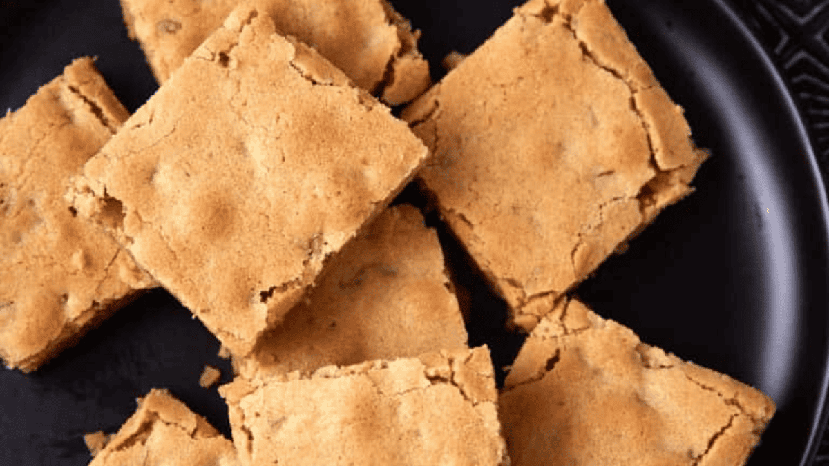 Several golden-brown blondies are arranged on a black plate. The squares have a slightly cracked surface and a chewy texture, making them an irresistible choice for Super Bowl desserts.