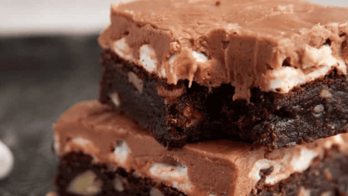 Two rich chocolate brownies stacked, each topped with a thick, creamy chocolate layer and marshmallow bits inside. These moist, fudgy treats with a smooth, glossy topping are perfect for anyone seeking easy brownie recipes.