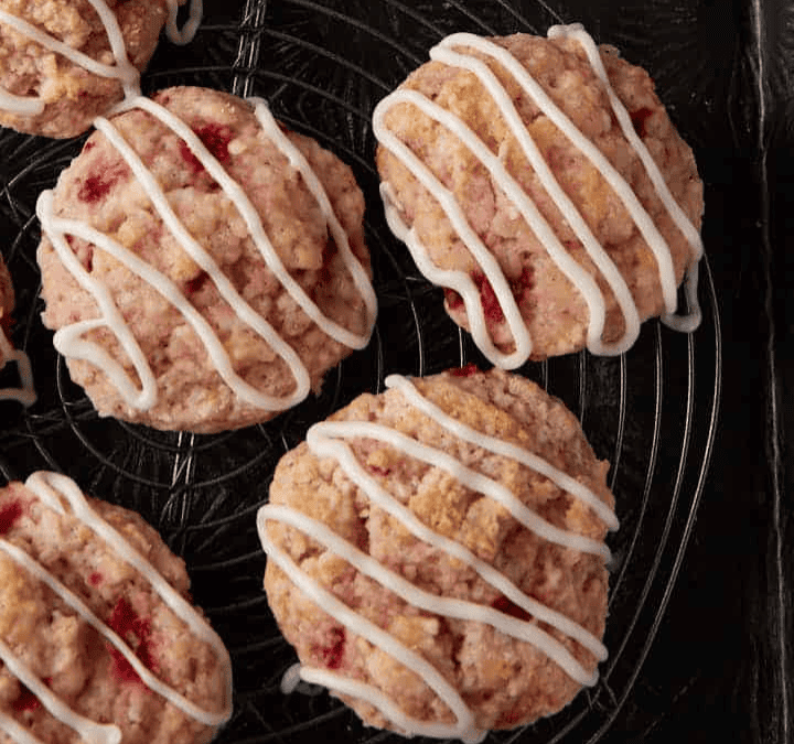 Five strawberry scones topped with white icing drizzle are arranged on a round cooling rack—a delightful quick dessert, with part of a gray cloth napkin visible to the side.