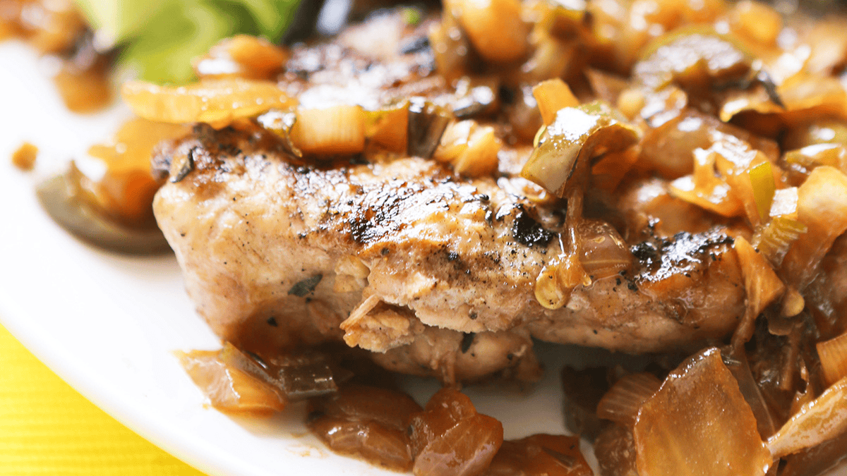A close-up of a grilled chicken breast topped with cooked, diced onions and peppers on a white plate, perfect inspiration for flavorful chicken thighs recipes.