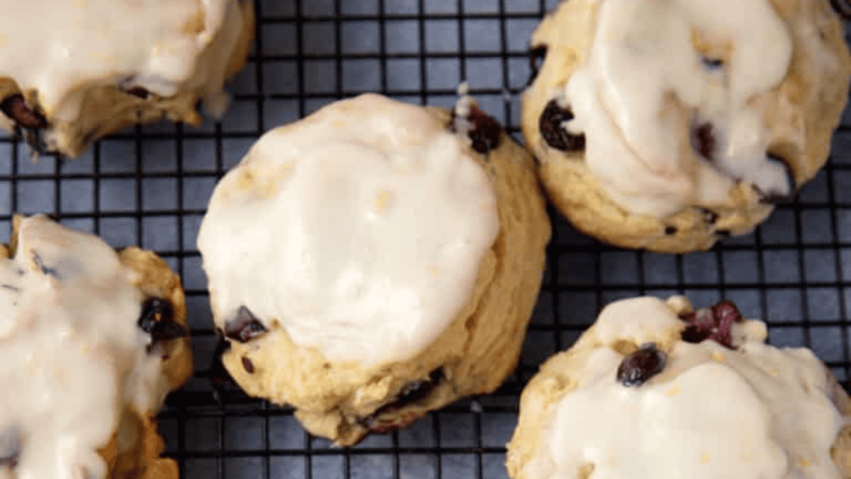 Iced scones with visible raisins or currants cool on a black wire rack, viewed from above. With their light golden color and white glaze, these treats will inspire blueberry recipes and more for your next baking session.