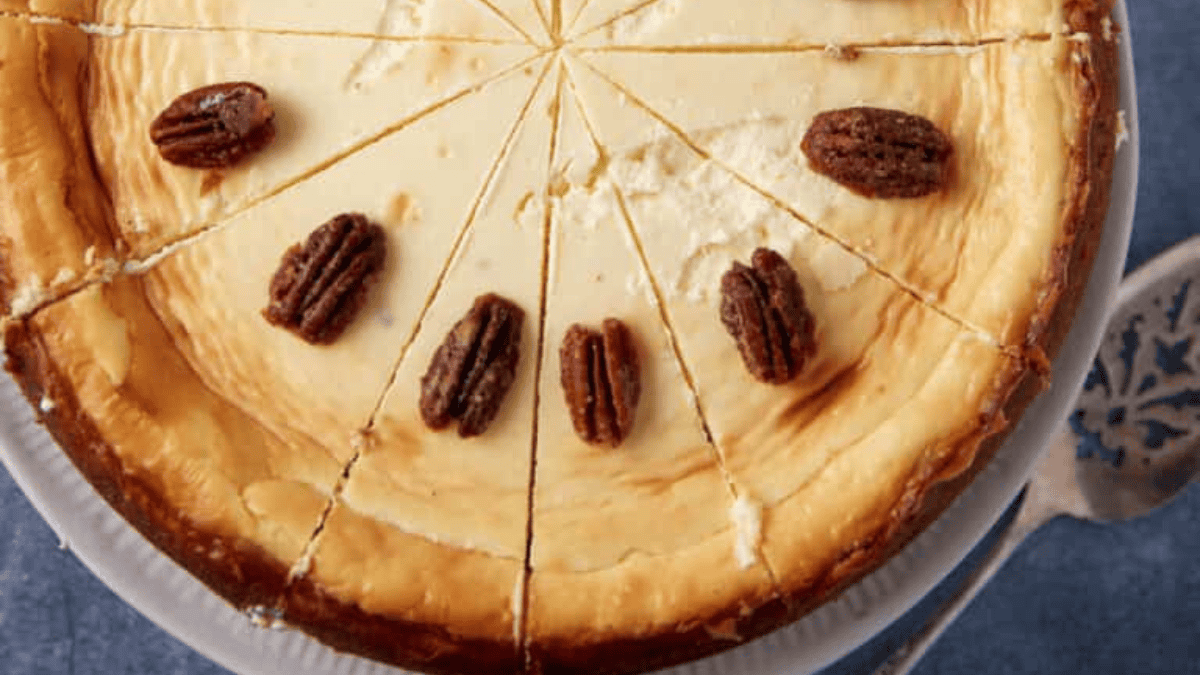 A cheesecake sliced into twelve pieces, decorated with whole pecans on several slices, displayed on a white plate—a delicious example for anyone seeking unique cheesecake ideas.