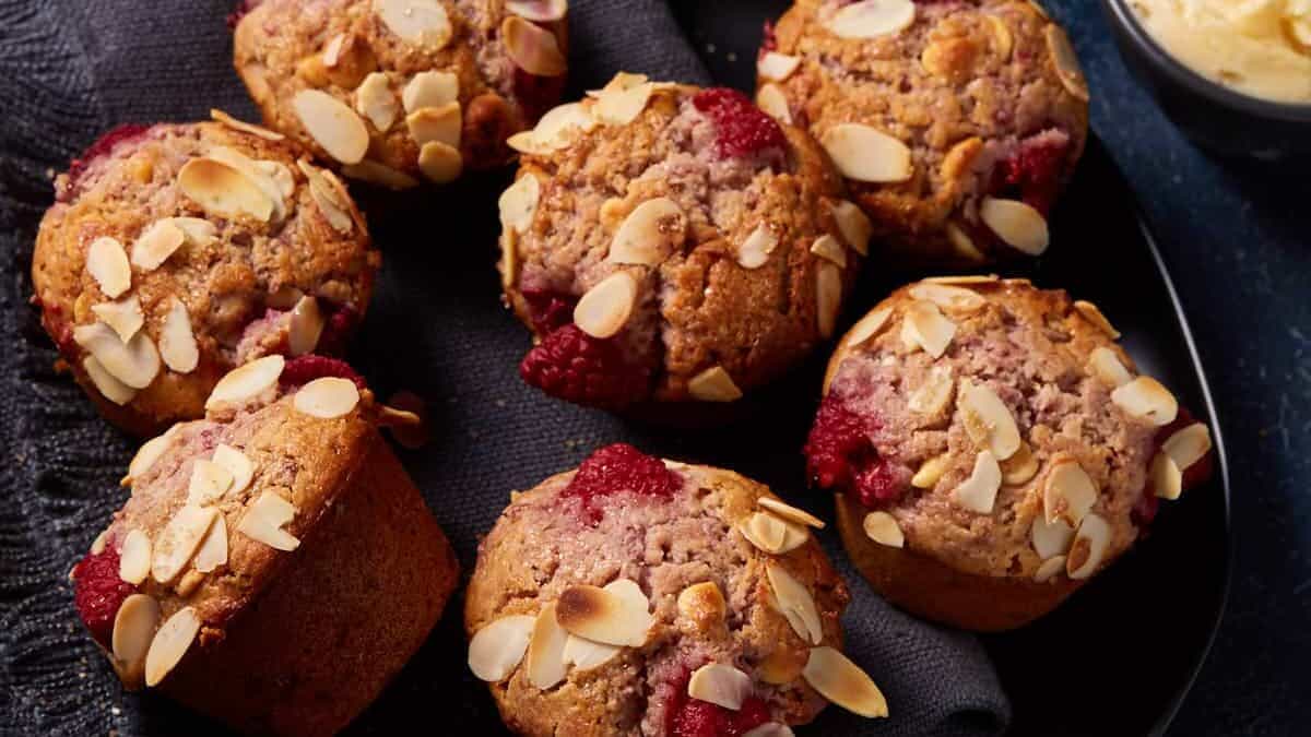 A platter of raspberry white chocolate muffins with honey butter and a cup of coffee.