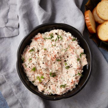 A bowl of cream cheese salmon dip next to a bowl of crostini.