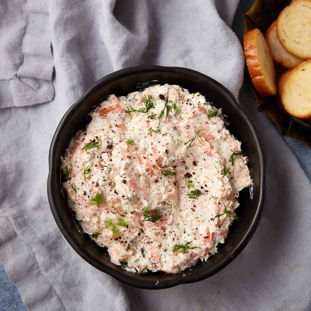 A bowl of cream cheese salmon dip next to a bowl of crostini.
