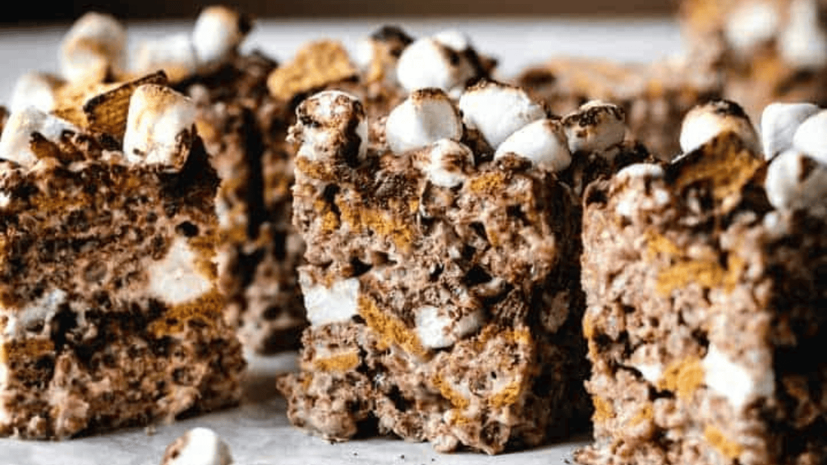 Close-up of several rice krispie treats made with chocolate, crispy rice cereal, mini marshmallows, and graham cracker pieces, arranged on parchment paper.