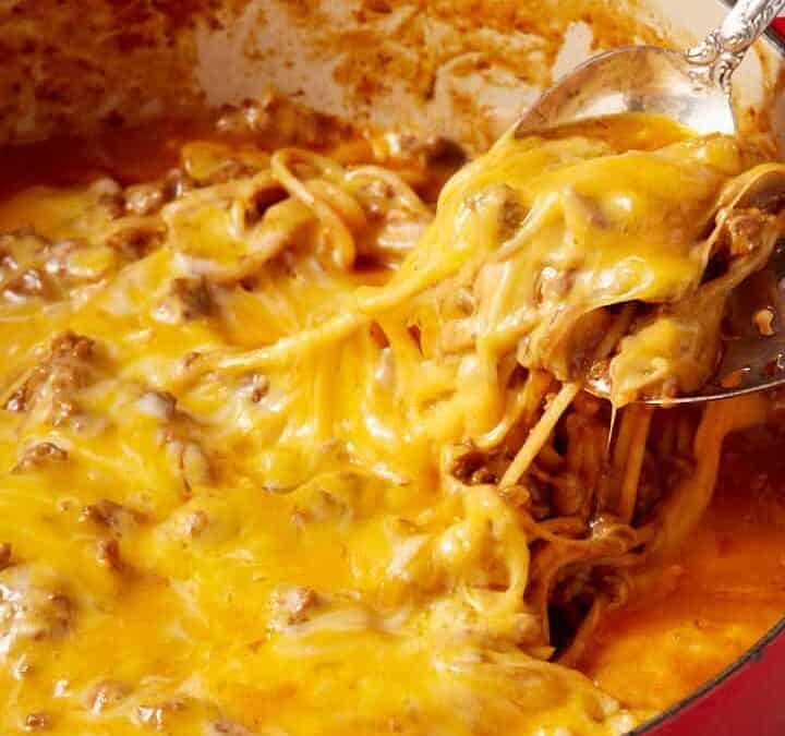 Cheese being pulled from a pot of spaghetti with two spoons.