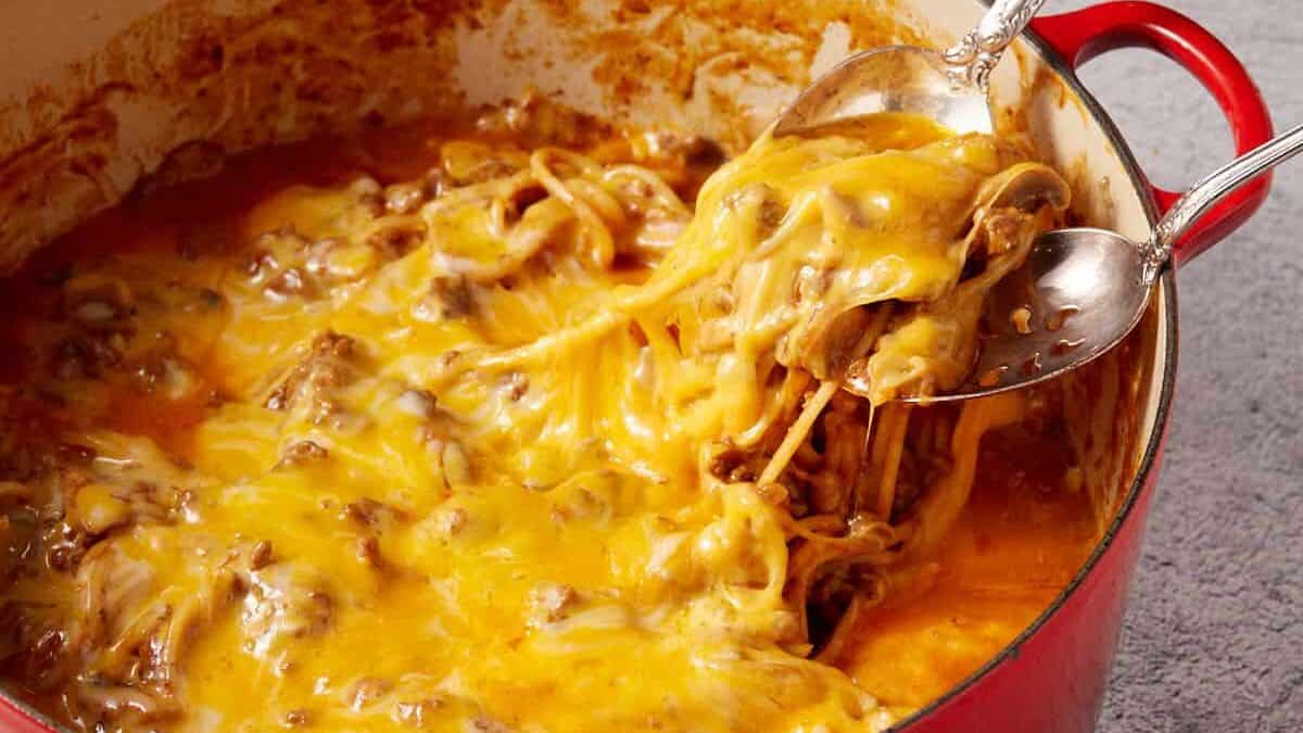 Cheese being pulled from a pot of spaghetti with two spoons.